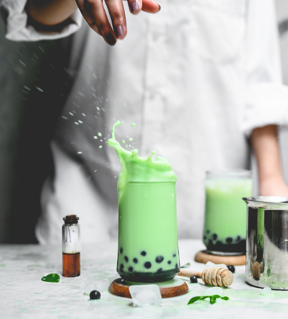 Green Matcha bubble tea being poured into a glass with a blurred background