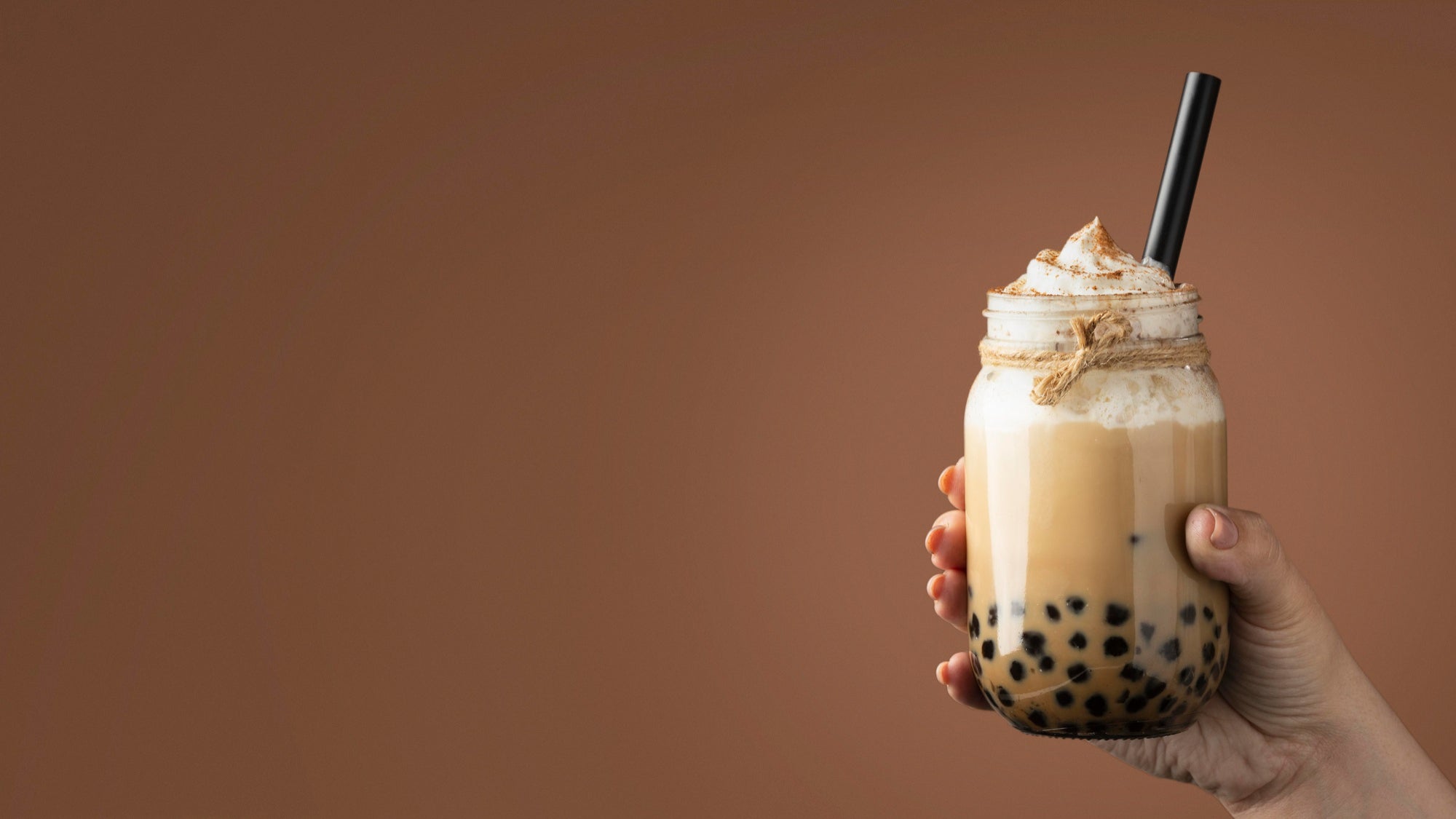 Hand holding a bubble tea with whipped cream against a brown background